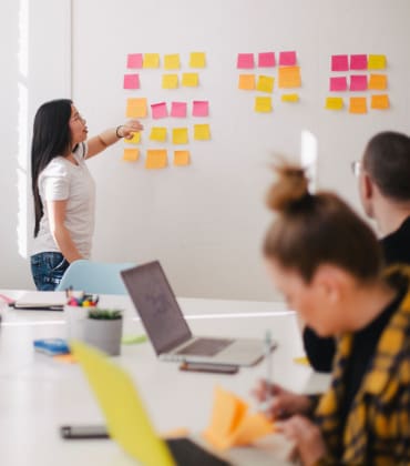 Groep mensen die kijken naar een vrouw  die voor een bord met post-its staat