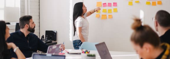 Groep mensen die kijken naar een vrouw die voor een bord met post-its staat