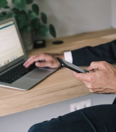 Iemand met telefoon in de hand en de andere hand op de laptop