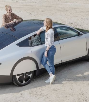 2 vrouwen praten met elkaar, leunend op een auto op zonne-energie