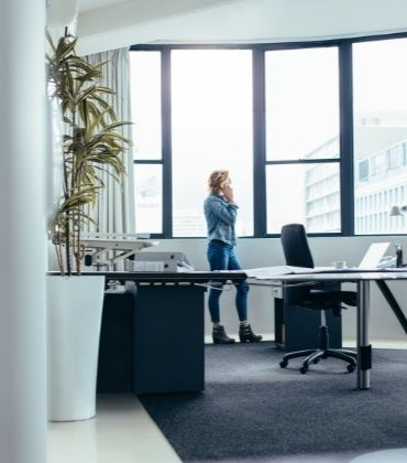 Vrouw staat bellend voor het raam in een kantoor