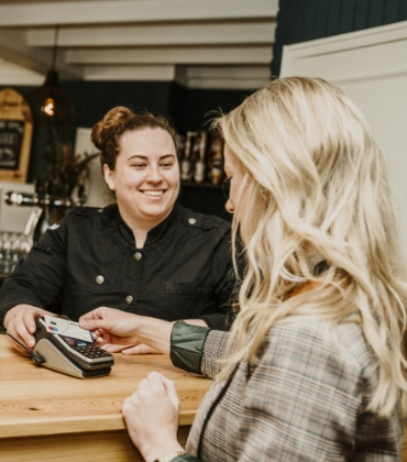 Een klant van een horeca-gelegenheid rekent met haar pinpas af bij een vrolijk lachende medewerker.