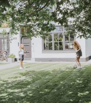 2 kinderen spelen op een zonnige dag in de tuin met een voetbal.