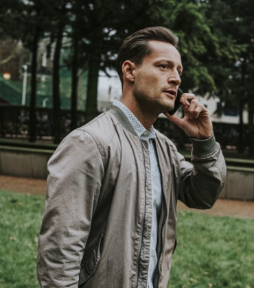 Een man staat met een telefoon aan zijn oor in een park
