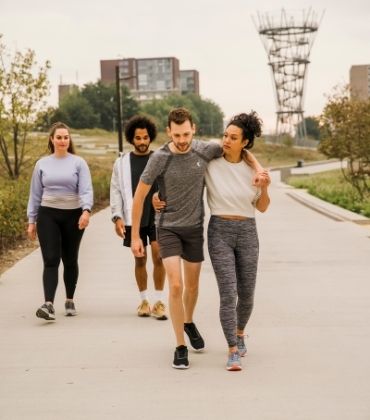 Een groepje van 4 mensen loopt in sportieve kleding door een park.