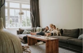 Een vrouw zit samen met 2 kinderen en een hond ontspannen op een bank in de woonkamer.