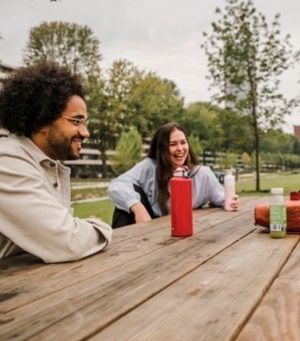 Een groepje jonge mensen zit bij elkaar aan een houten picknicktafel in een stadspark.
