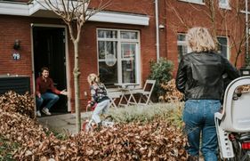 Een kind fietst van een vrouw op de fiets naar een man die op zijn hurken in de deuropening zit