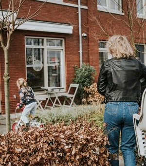 Een kind fietst van een vrouw op de fiets naar een man die op zijn hurken in de deuropening zit
