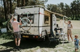 Man haalt fiets van de camper en vrouw hangt lampjes op aan het luifel van de camper.