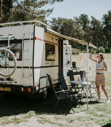 Man haalt fiets van de camper en vrouw hangt lampjes op aan het luifel van de camper.