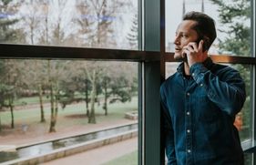 Een man staat te bellen bij het raam en kijkt naar buiten
