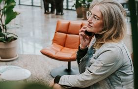 Vrouw zit met de telefoon aan haar oor in een kantoorhal.