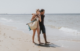 Een man en vrouw lopen op het strand, de man heeft zijn arm om de schouder van de vrouw