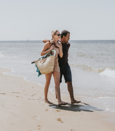 Een man en vrouw lopen op het strand, de man heeft zijn arm om de schouder van de vrouw