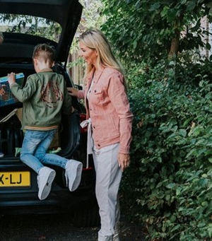 Vrouw staat bij auto met spullen achterin en kind zit op de rand van de kofferbak