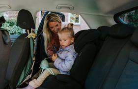 Vrouw zet een kind in een kinderstoel op de achterbank van een auto