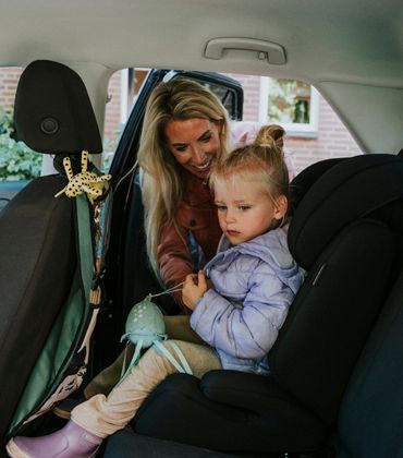 Vrouw zet een kind in een kinderstoel op de achterbank van een auto