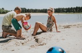 Een zomerse dag; een gezin geniet op een strandje van de zon, en van het spelen met zand en water.