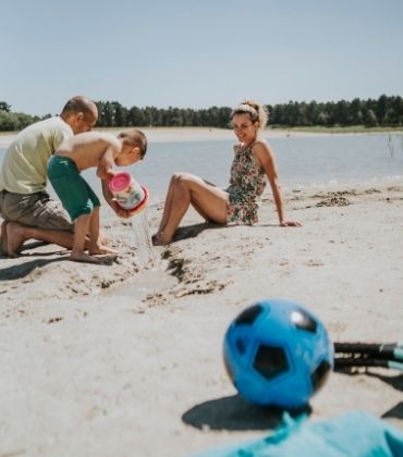 Een zomerse dag; een gezin geniet op een strandje van de zon, en van het spelen met zand en water.