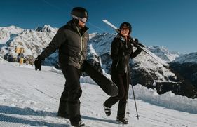 Man en vrouw lachend op de piste. Goed voorbereid op wintersport.