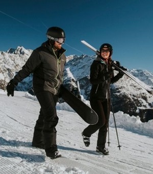 Man en vrouw lachend op de piste. Goed voorbereid op wintersport.