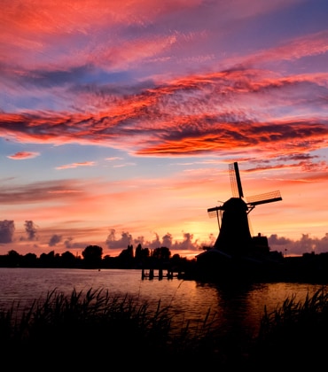 Een Hollands landschap met een molen, in het avondrood