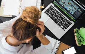 Vrouw die  voor haar laptop zit met haar hoofd in haar handen