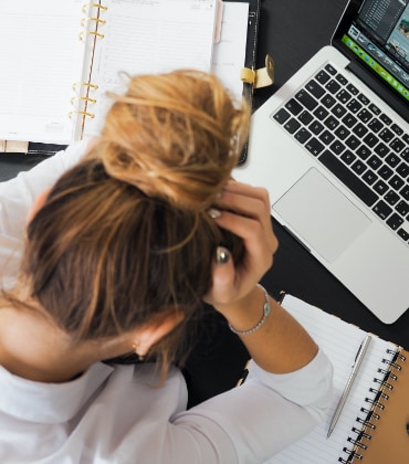 Vrouw die  voor haar laptop zit met haar hoofd in haar handen