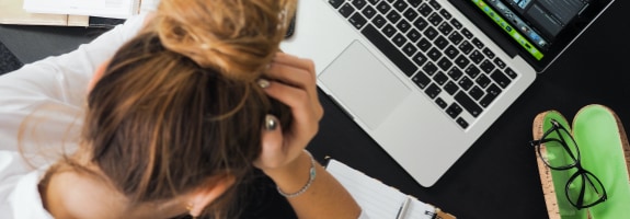 Vrouw die voor haar laptop zit met haar hoofd in haar handen