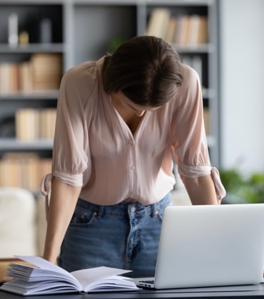 Vrouw die voor haar laptop staat met haar hoofd gebogen