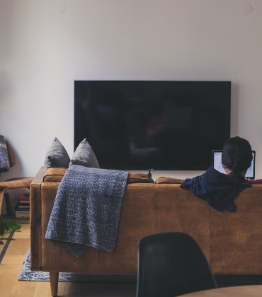 woonkamer met televisie en bank waarop iemand op zijn laptop werkt