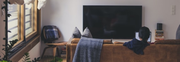 woonkamer met televisie en bank waarop iemand op zijn laptop werkt