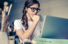 Een vrouw die achter haar laptop zit en met haar ogen fronst