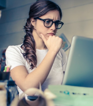 Een vrouw die achter haar laptop zit en met haar ogen fronst