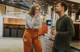 Een man en vrouw staan bij een koffieapparaat en drinken samen een kopje koffie.