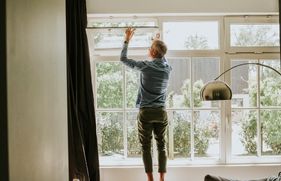 Man staat op kruk bij raampartij en opent kiepraam
