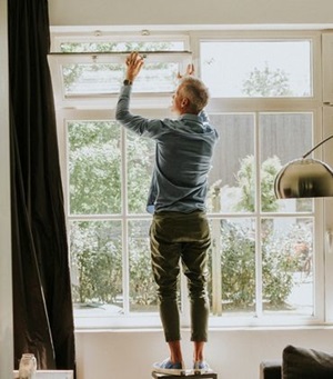 Man staat op kruk bij raampartij en opent kiepraam