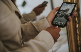 Een persoon houdt een mobiele telefoon in de hand, en steekt de oplaadkabel met de andere hand in de oplaadpoort van het toestel.