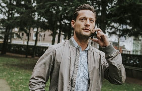 Een man staat in een tuin met een telefoon aan zijn oor.