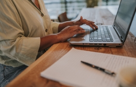 De handen van een persoon raken het toetsenbord van een openstaande laptop aan.