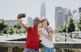 Man en vrouw staan op een brug, de man maakt een selfie, de vrouw heeft koffie in haar hand