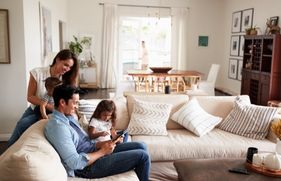 Man, vrouw en 2 kindjes zitten in een gezellig huis op de bank en kijken naar de iPad