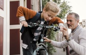 Vader en zoon houden samen een kinderfiets vast.