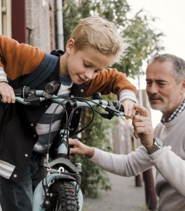 Vader en zoon houden samen een kinderfiets vast.