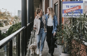 2 vrouwen staan samen met hun hond voor hun nieuwe huurappartement.