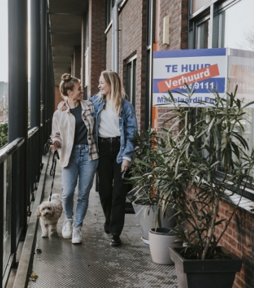 2 vrouwen staan samen met hun hond voor hun nieuwe huurappartement.