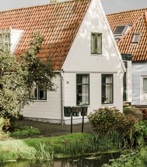 Een huis bekleed met wit hout en veel groen er omheen