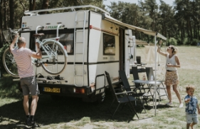 Stel is op reis met de camper. Vrouw hangt lampjes op en man haalt de fietsen van het rek.