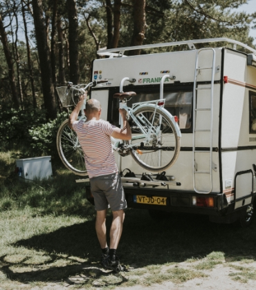 Stel is op reis met de camper. Vrouw hangt lampjes op en man haalt de fietsen van het rek.